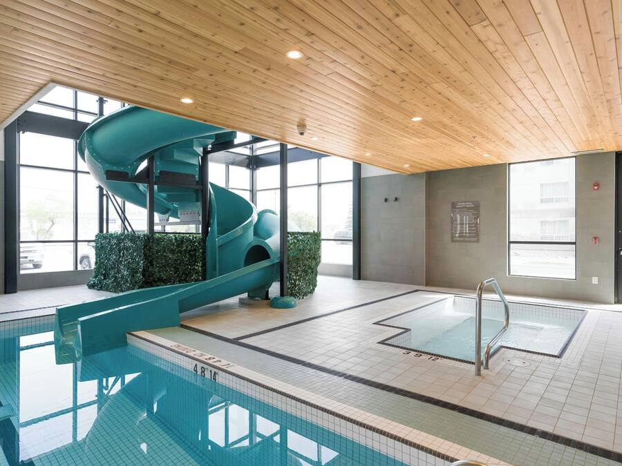 An indoor swimming pool with a slide, wooden ceiling, and safety rules posted on the wall.