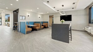 Un espace d’accueil moderne avec un comptoir noir, des sièges dotés de coussins bleus et bruns, un téléviseur fixé au mur et un éclairage encastré au plafond.