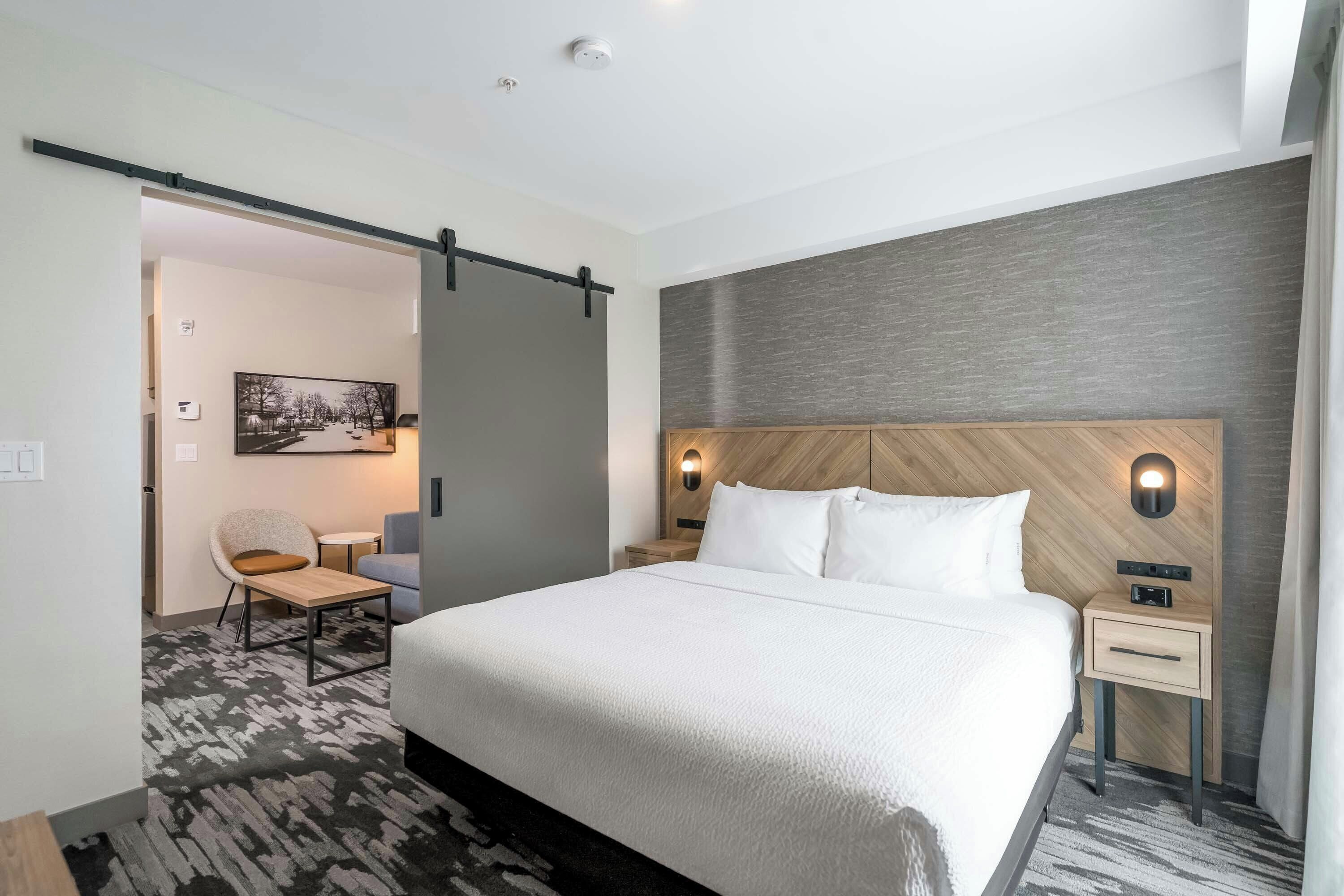 Une chambre d’hôtel avec un lit, un bureau, une chaise, un tableau et une porte coulissante.