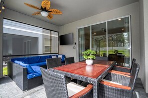 An outdoor patio with a wooden table, wicker chairs, a blue sofa, and a ceiling fan.