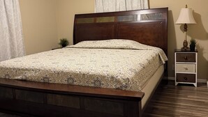 Un dormitorio con una cama de madera, una mesita de noche con lámpara, una planta pequeña y una alfombra estampada.