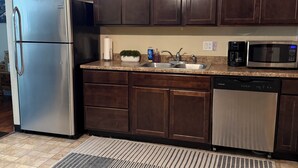 Una cocina con armarios de madera oscura, electrodomésticos de acero inoxidable, encimera de granito y una alfombra estampada.