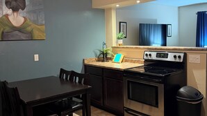 Una cocina con una mesa de comedor, sillas, estufa, ventilador de techo y un cuadro en la pared.