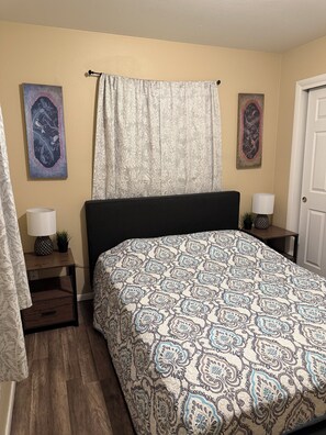 Una camera da letto con una coperta a motivi, due lampade a parete, un comodino con una pianta e due opere d'arte incorniciate alle pareti.