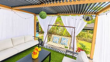 An outdoor seating area with a swing, a sofa, and a table with flowers.