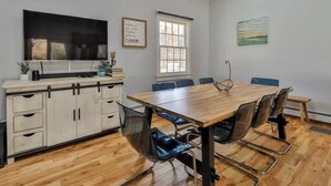 Una cocina moderna con una televisión grande, armarios de madera y una zona de comedor con mesa y sillas de madera.