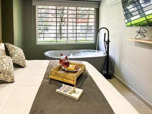 A bedroom with a large window, a bathtub, and a tray with wine glasses and bread. - Stylish urban loft in Medellín | Con Aire 1-01 (Medellín)