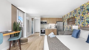 A modern hotel room with a large bed, a dining area with a table and chairs, a kitchenette, and a colorful wall mural. - Marine Surf by Tropical Escapes Realty (Honolulu)