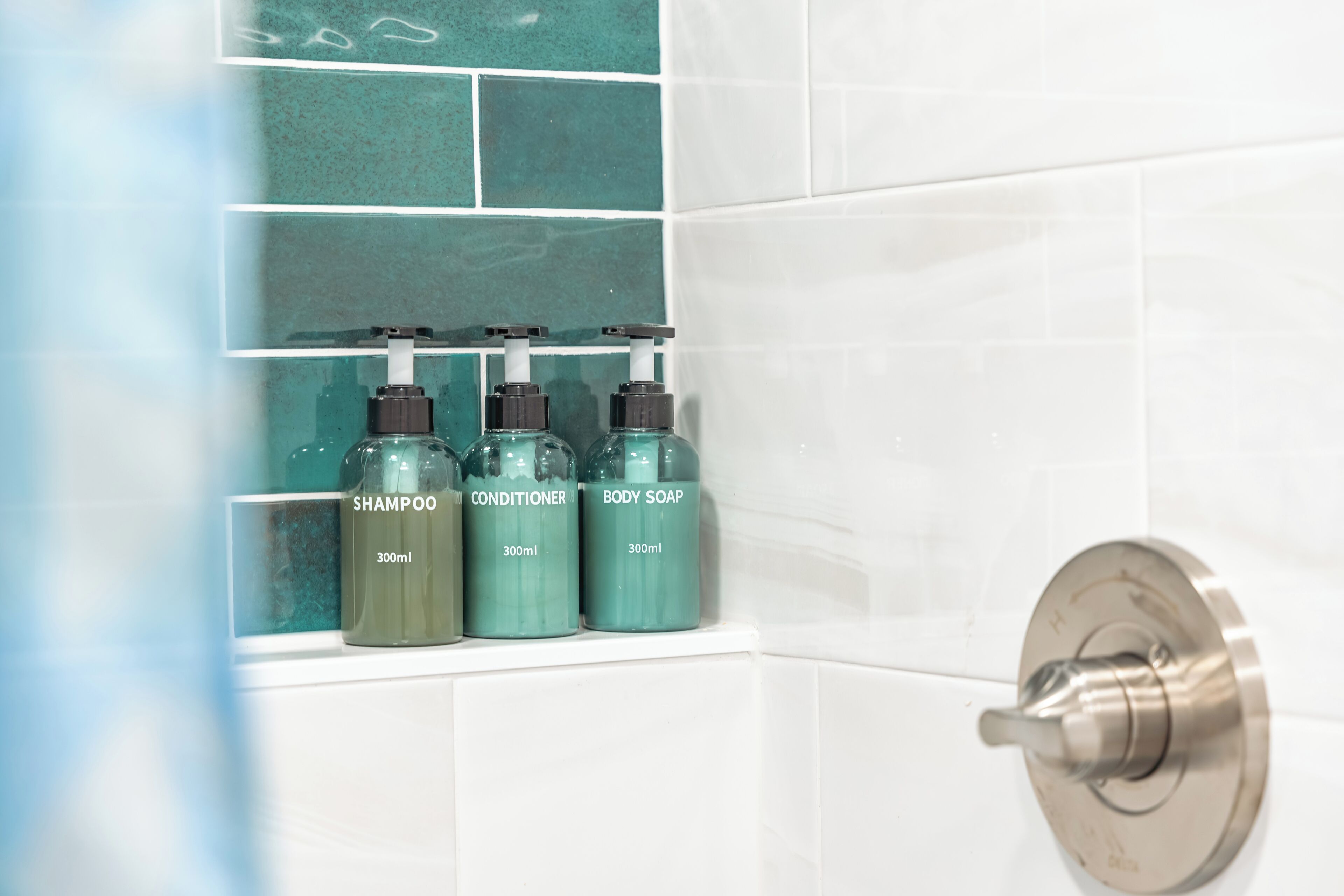 A bathroom with three bottles of personal care products on a shelf.
