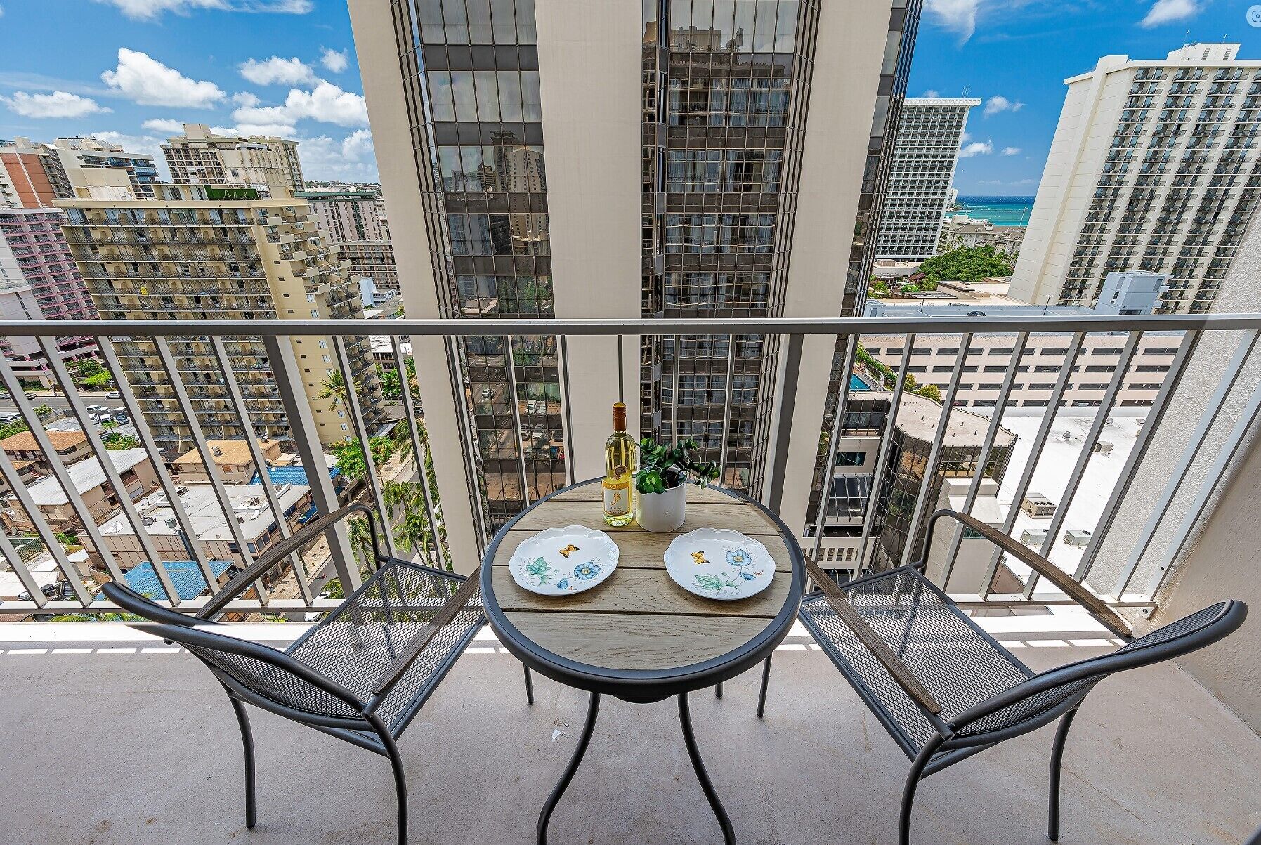 Un balcon avec deux chaises et une table, donnant sur un paysage urbain avec de hauts immeubles et une piscine.