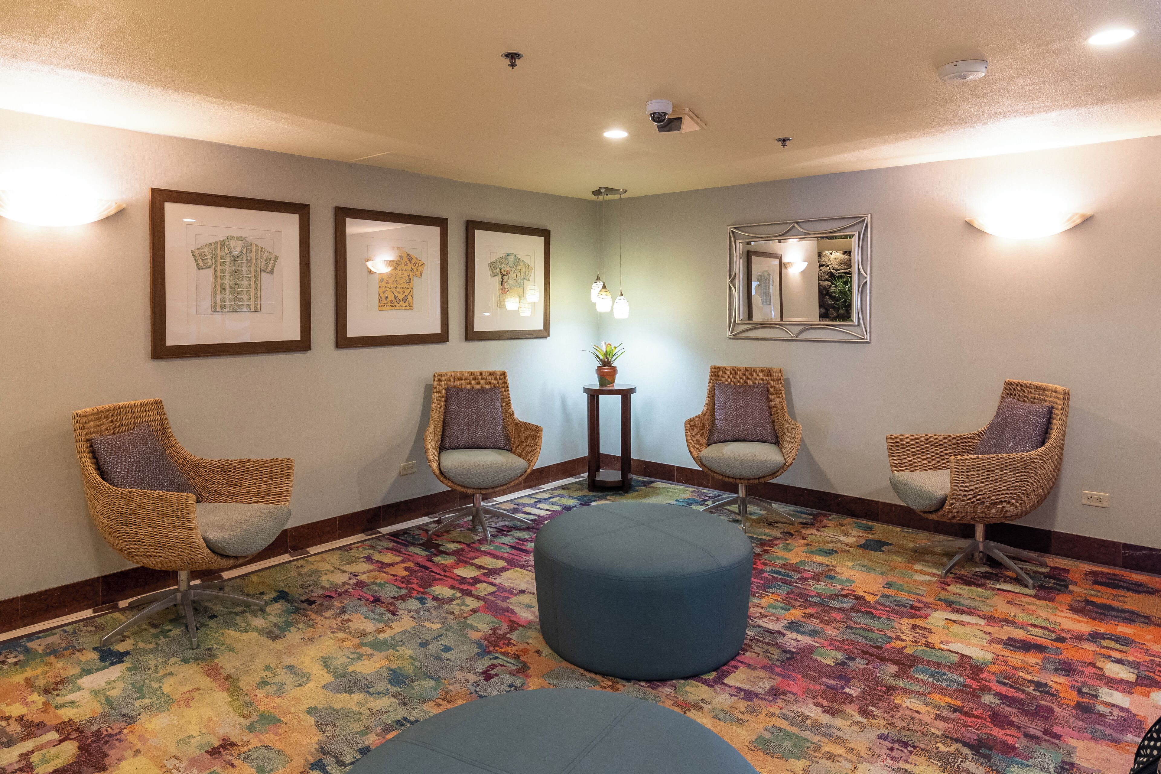 A waiting area with wicker chairs, a colorful patterned carpet, framed artwork on the walls, and a small table with a plant.