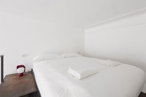 A neatly made bed with white linens and a folded towel on a wooden nightstand.