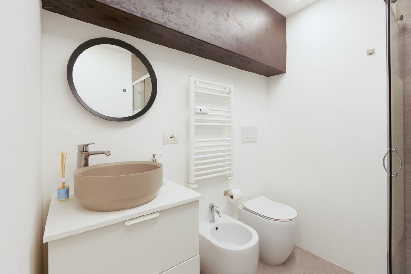 A modern bathroom with a round sink, a toilet, a bidet, a towel rack, and a mirror.