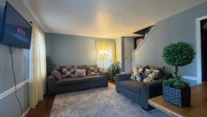 A living room with a grey sofa, a smaller armchair, a coffee table, a TV mounted on the wall, and a staircase leading to another level. - Charming 3-bedroom house with WiFi and AC in Arlington (Arlington)