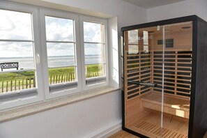 Une pièce dotée d’une grande fenêtre donnant sur un espace verdoyant et un plan d’eau, d’un banc en bois et d’un espace clos par des parois de verre avec un plancher en bois.