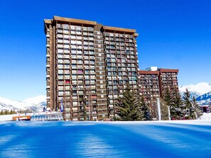Un hotel de varios pisos con numerosas balconadas, un paisaje de estación de esquí y un cielo azul despejado.