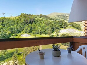 Ein Balkon mit Blick auf eine grüne Landschaft, ein Tisch mit Pflanze und Tasse sowie ein Stuhl.