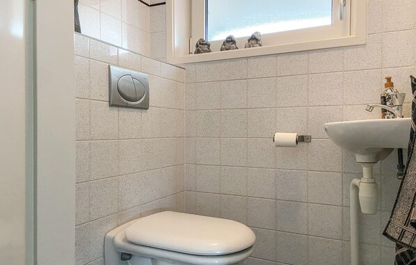 A small, modern bathroom with a toilet, a sink, and a window above the toilet.