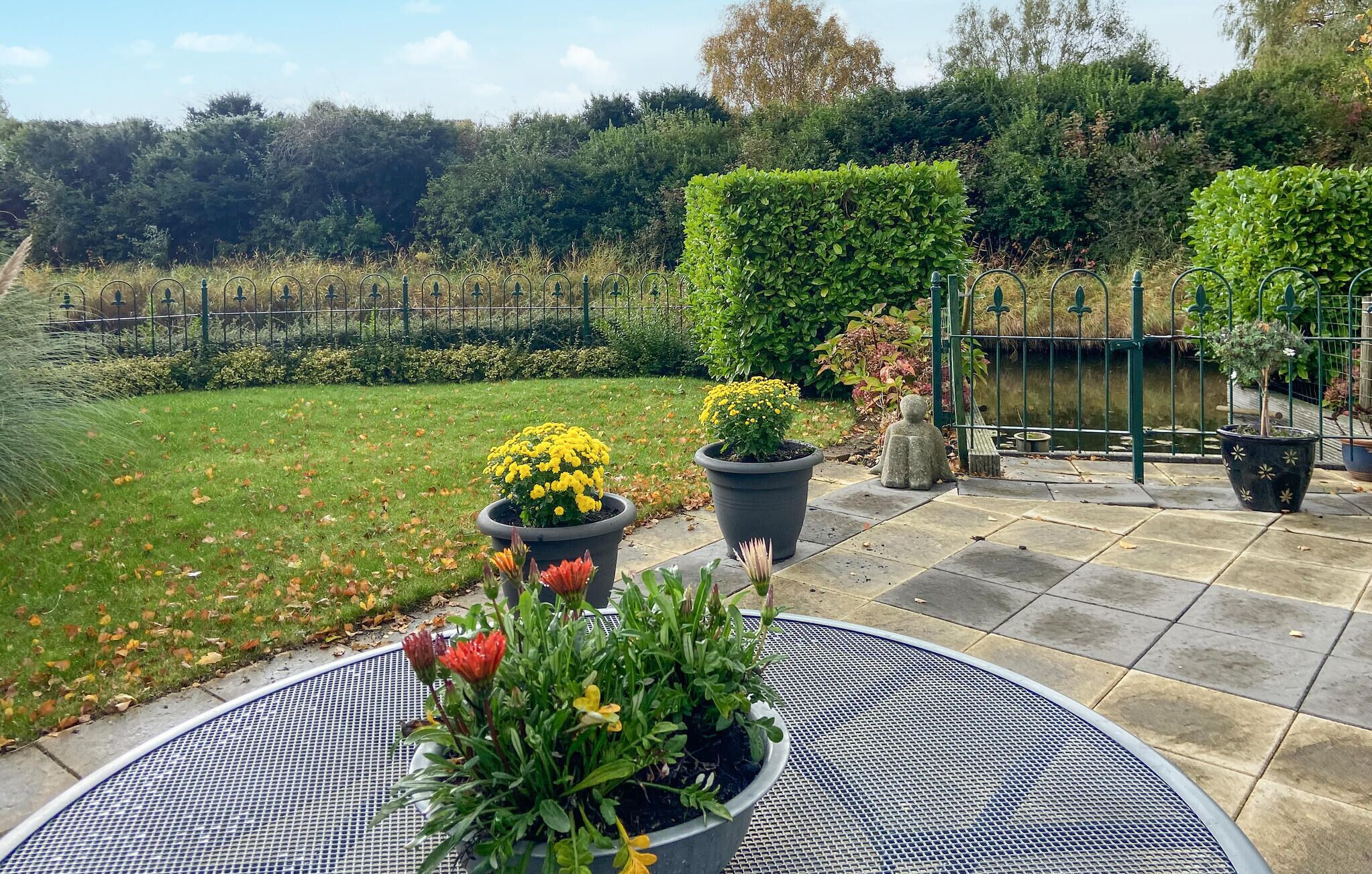 Eine Terrasse mit einem runden Metalltisch, Topfpflanzen und einem Kiesweg.