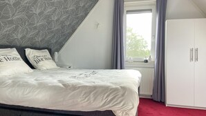 A bedroom with a bed, a wardrobe, a window with curtains, and a radiator. - Pet friendly home in Opperdoes (Opperdoes)