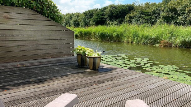 A wooden deck with two planters and a view of a river with lily pads. - Pet friendly home in Opperdoes (Opperdoes)
