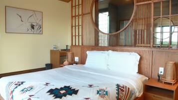 A bedroom with a large bed, a wooden headboard with a mirror, a bedside table with a lamp, and a wall-mounted artwork.