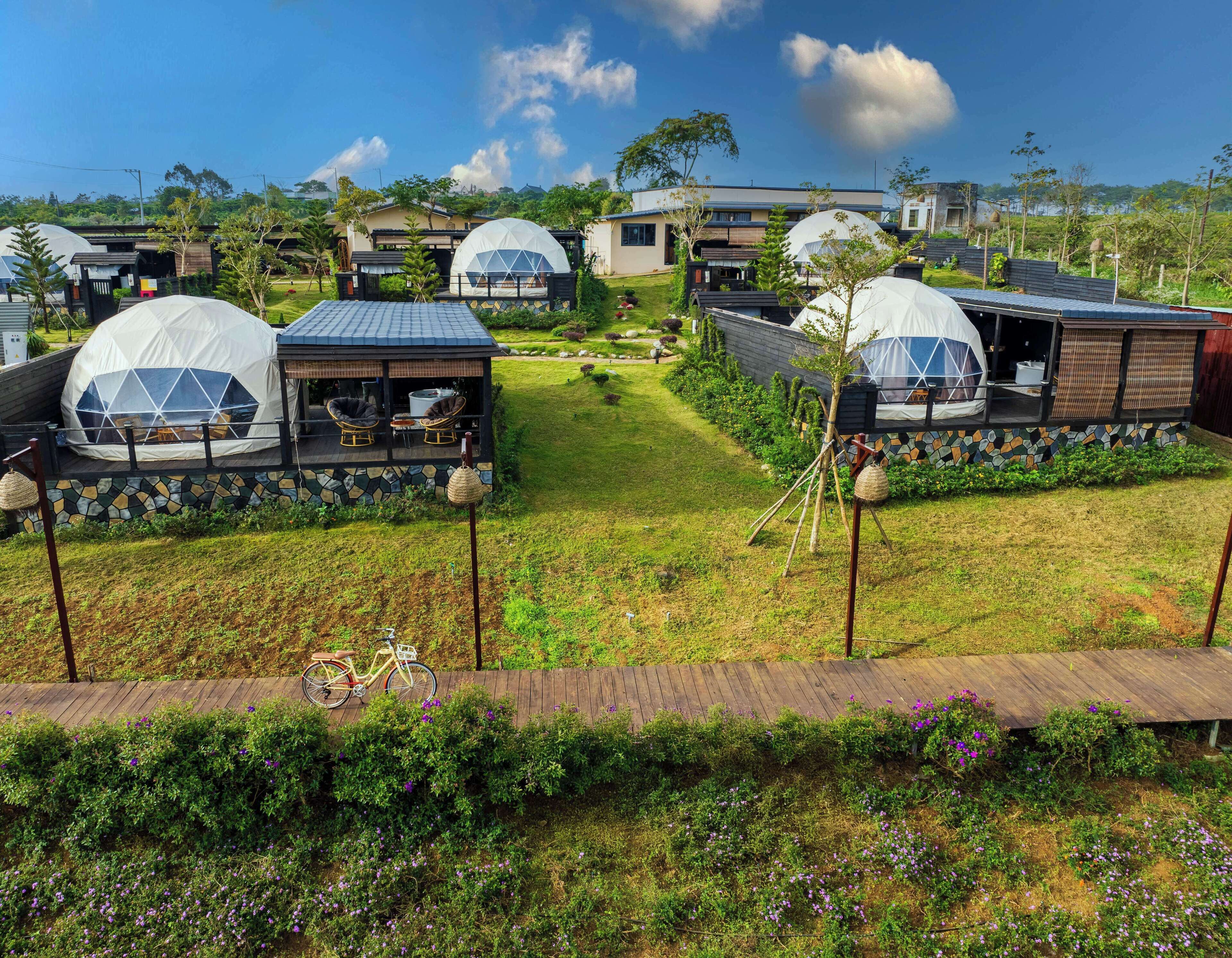 A series of dome-shaped accommodations with outdoor seating areas, surrounded by well-maintained gardens and a clear sky.