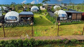 A series of dome-shaped accommodations with outdoor seating areas, surrounded by well-maintained gardens and a clear sky.