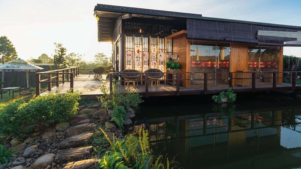 A modern houseboat with a wooden deck, outdoor seating, and a view of the water. - Olala Glamping (Bao Lam 1)
