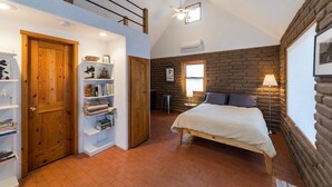 Un dormitorio con techo estilo loft, cama, estantería, escritorio y ventana con vistas.