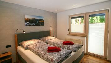 Ein Doppelbett mit floralem Bettbezug, ein Nachttisch, eine Wandlampe, ein Landschaftsbild und ein Fenster mit Jalousien.