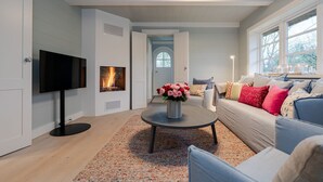Una sala de estar moderna con chimenea, televisor, mesa de centro con un florero y sofá con cojines.