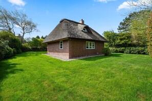 A single-story brick house with a thatched roof, surrounded by a well-maintained lawn and dense shrubbery.