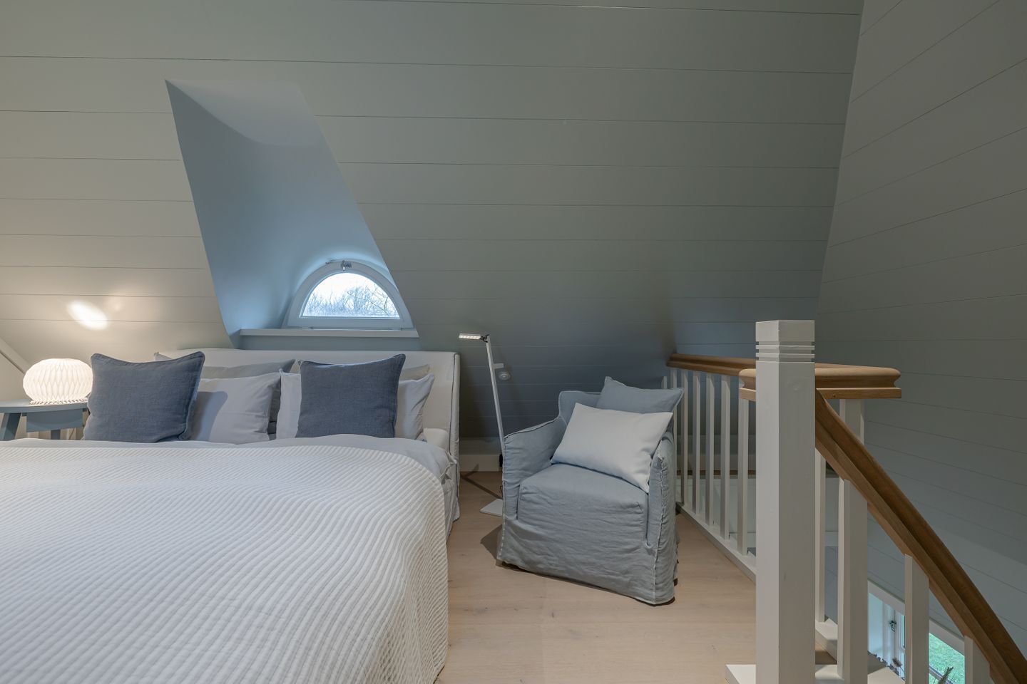 Een slaapkamer met een groot bed, een stoel, een nachtkastje, een lamp en een raam.