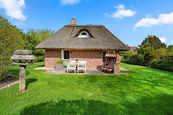 A thatched-roof house with a brick exterior, a small garden, and a flag in the background.