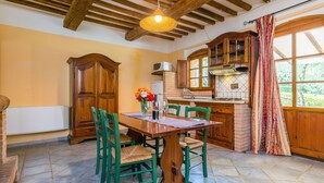 A rustic kitchen with a wooden table, green chairs, and a hanging light fixture.