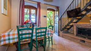 A dining area with a checkered tablecloth, green chairs, and a fireplace. - Nice apartment for 5 people with A/C, pool, WIFI, TV and patio (Riparbella)
