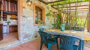 An outdoor patio with a stone wall, wooden beams, a table with chairs, and potted plants. - Nice apartment for 5 people with A/C, pool, WIFI, TV and patio (Riparbella)