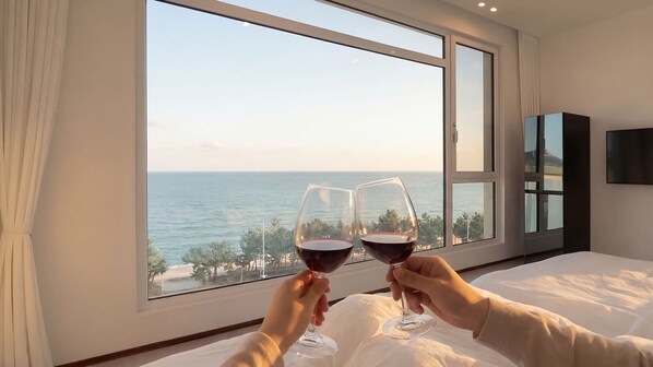 A room with a large window overlooking the sea, a bed, and a TV on the wall.