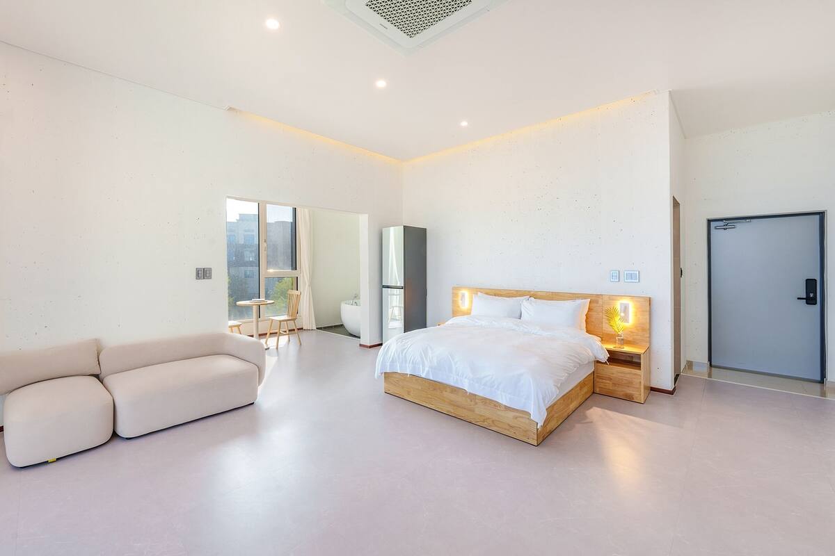 A modern hotel room with a large bed, a seating area, a bathroom, and a view of the city.