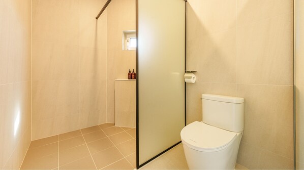 Un baño moderno con cabina de ducha de vidrio, inodoro y un estante pequeño con artículos de aseo.