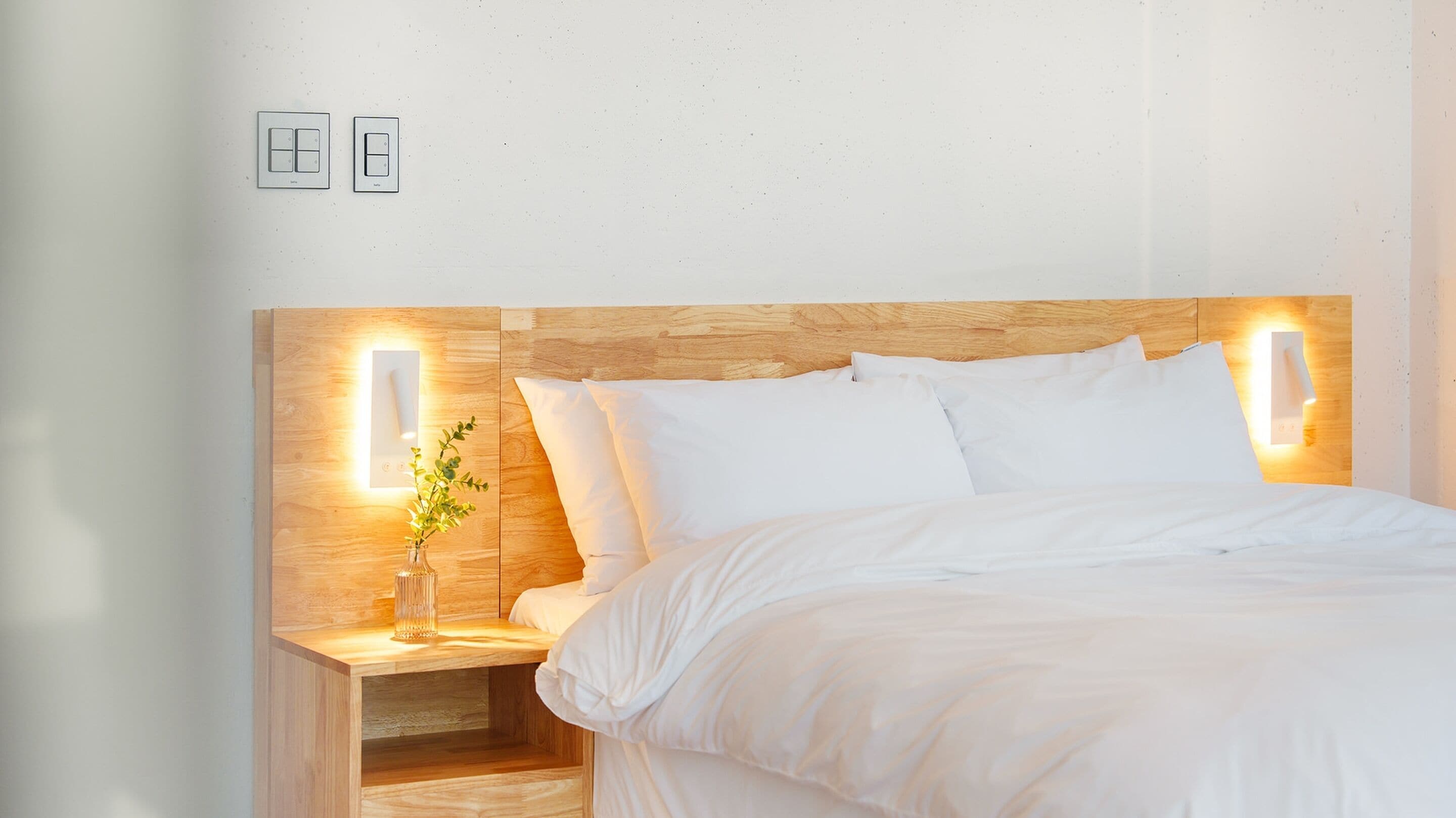 Una cama bien tendida con sábanas blancas, cabecera de madera y lámparas de noche.