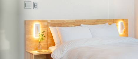 Una cama bien tendida con sábanas blancas, cabecera de madera y lámparas de noche.