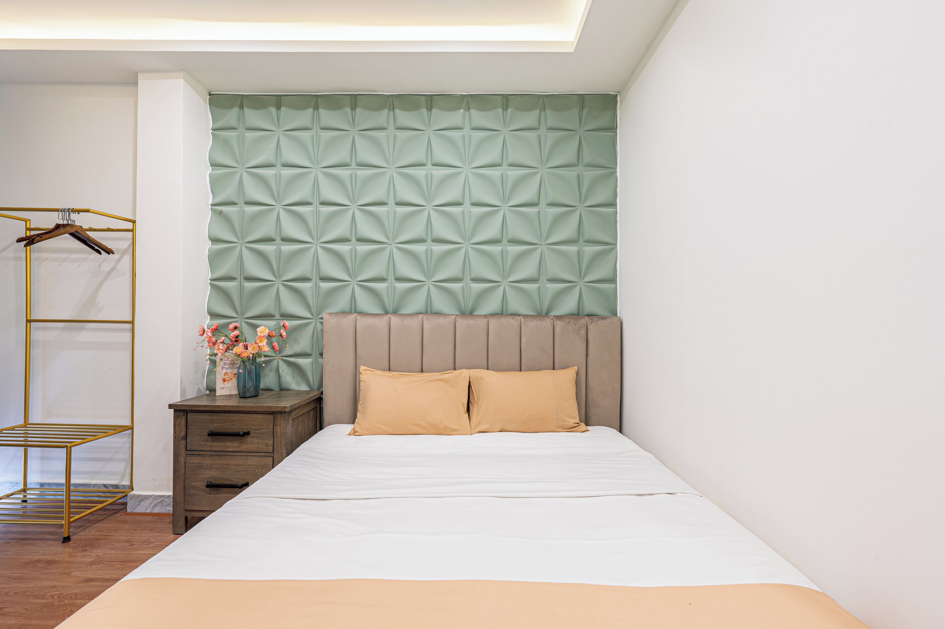 A neatly arranged bedroom with a bed, a nightstand, a hanging wardrobe, and a decorative vase.