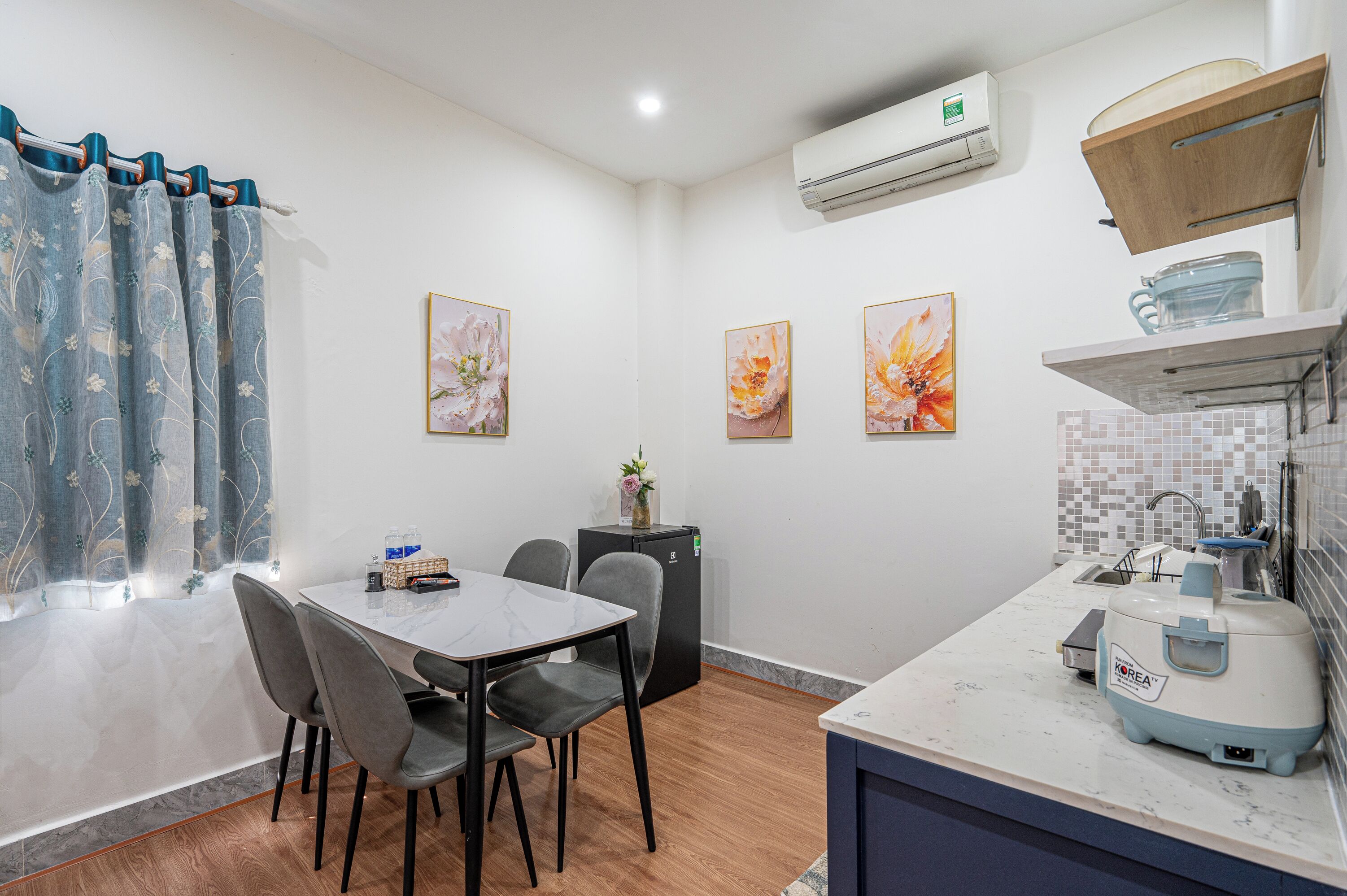 A compact kitchen with a refrigerator, sink, and a compact stove. There is a dining area with a table and chairs.