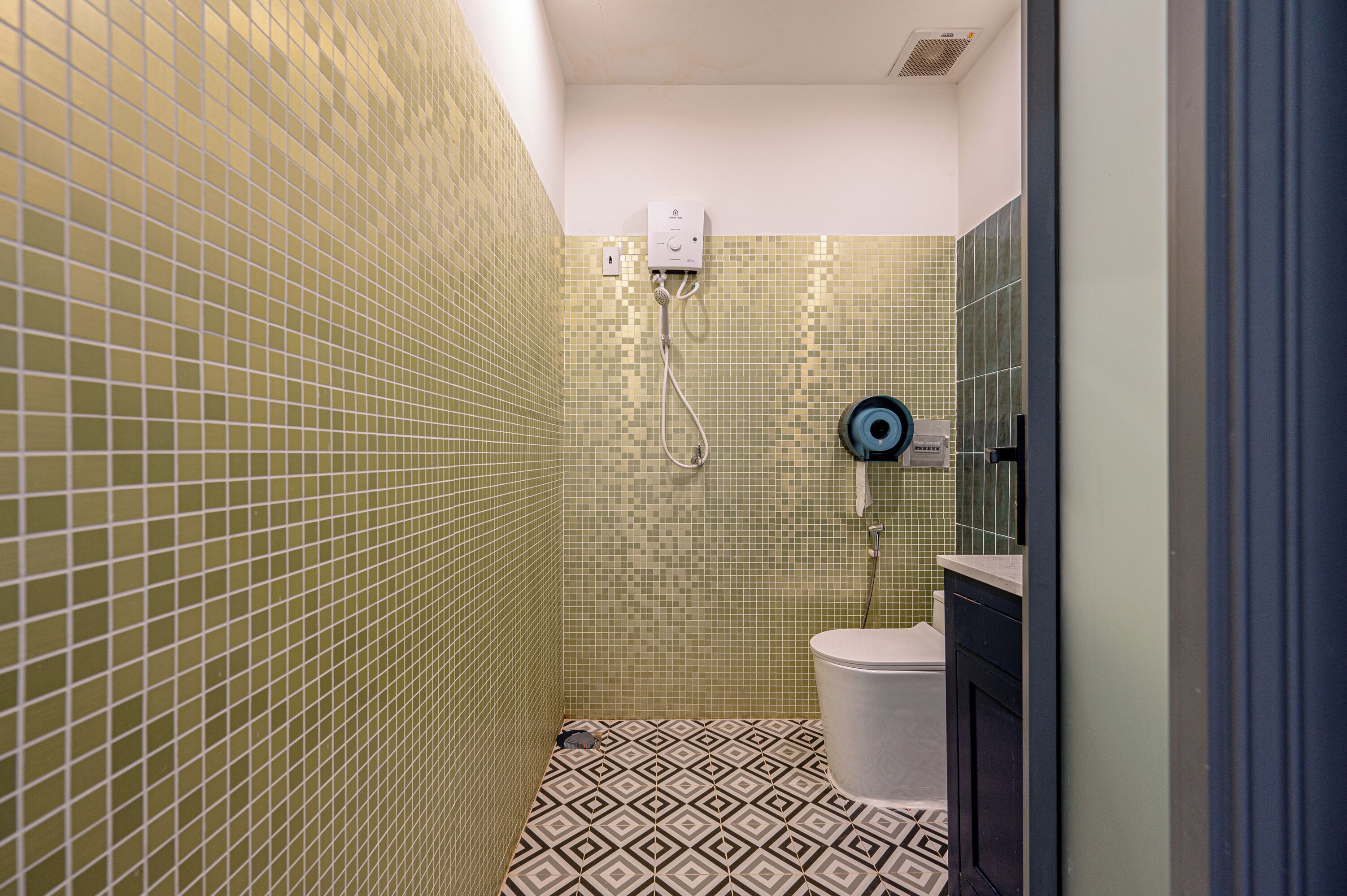 A bathroom with mosaic tile walls, a toilet, and a shower with a control panel.