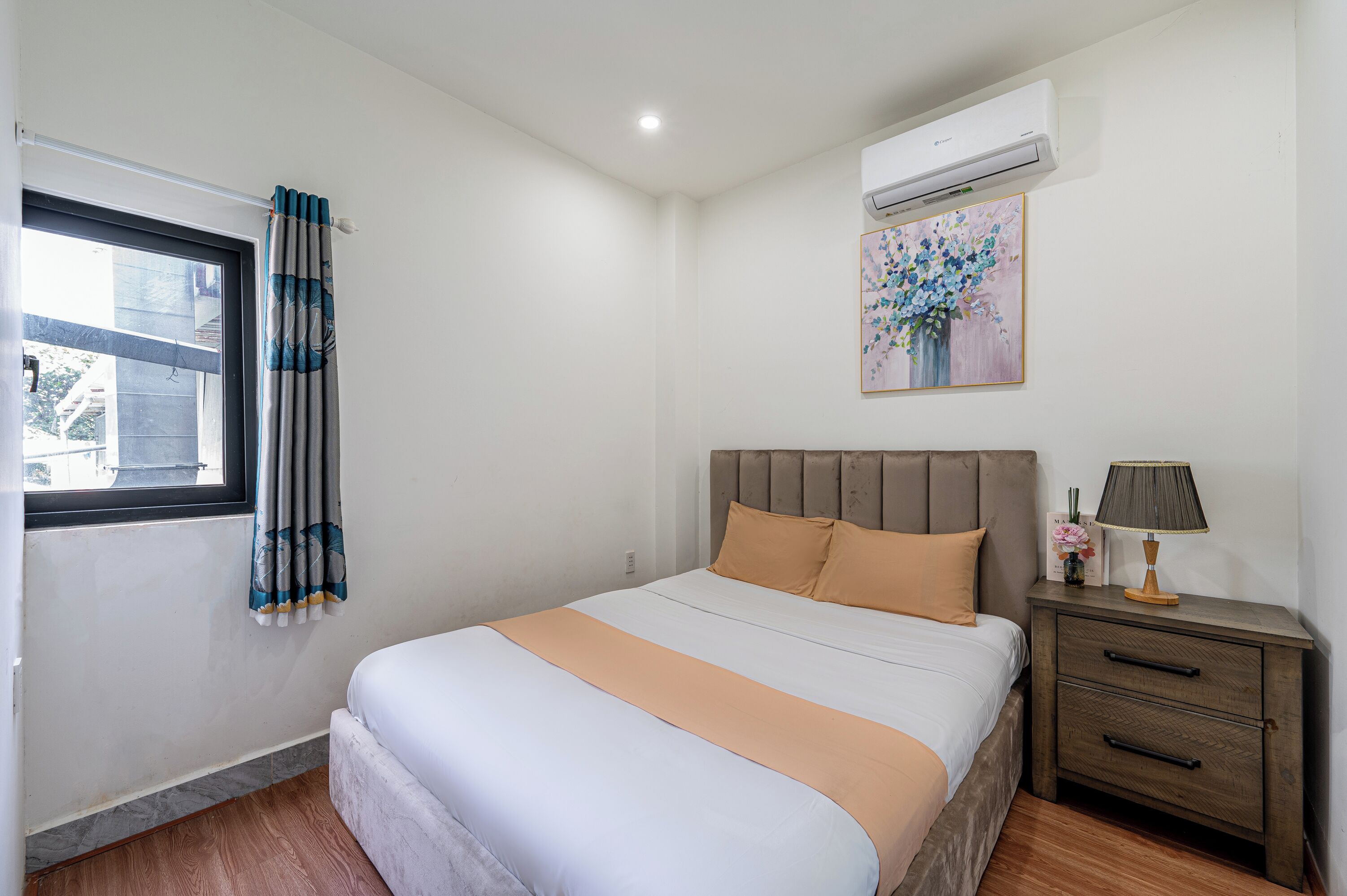 A bedroom with a bed, a nightstand, a lamp, an air conditioner, and a window with curtains.
