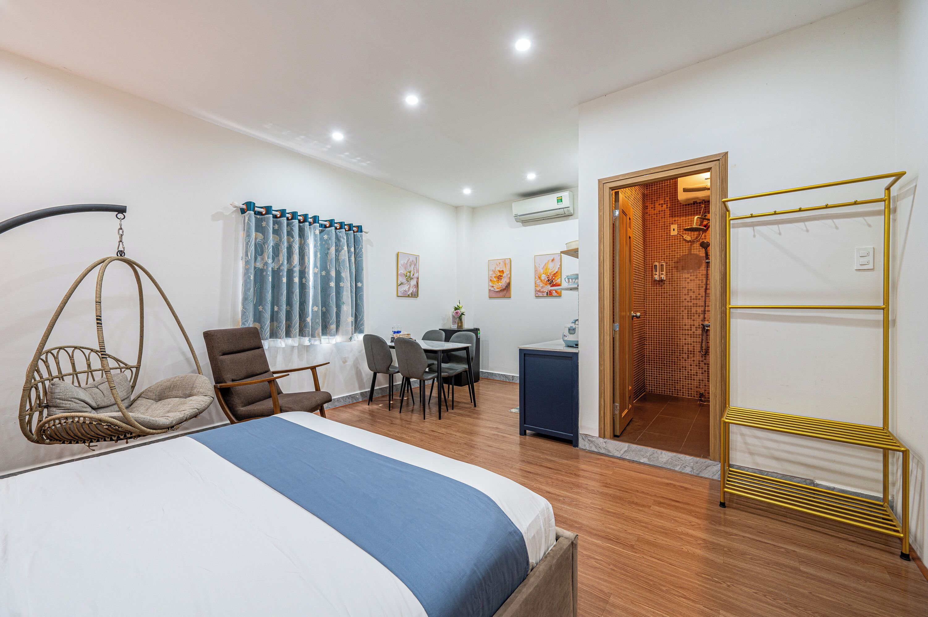 A hotel room with a bed, a dining table with chairs, a hanging chair, a small desk, and a shower area.