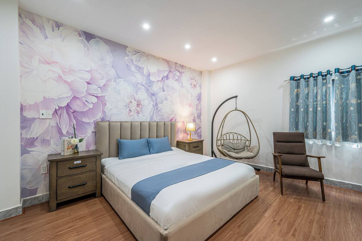 A bedroom with a bed, a nightstand, a chair, a hanging chair, and a window with curtains.