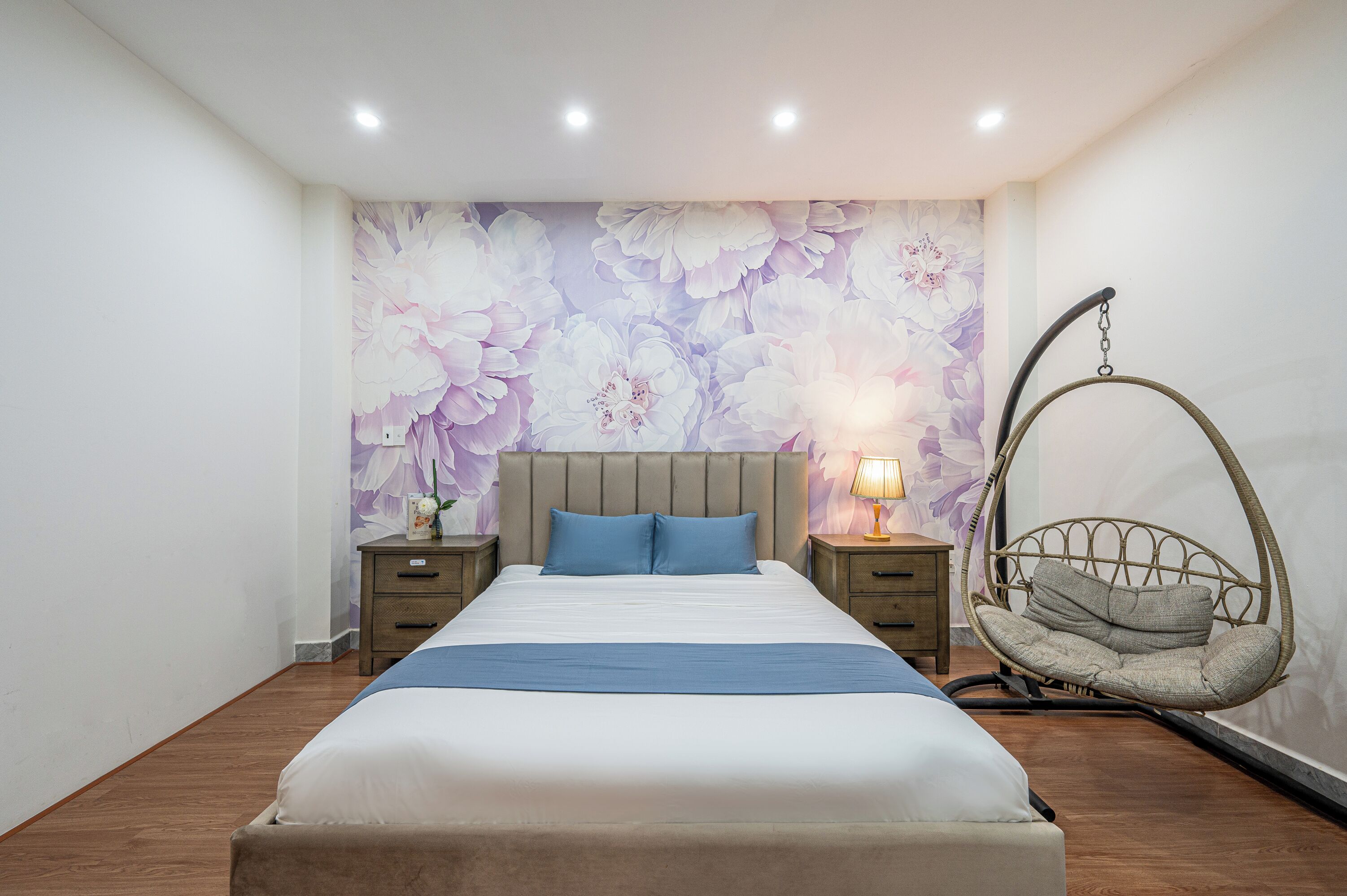 Un dormitorio con cama, mesitas de noche, una silla colgante y un papel tapiz floral.
